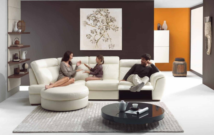 salon moderno, padres y niña, sofá blanco de piel, salón con paredes color marrón y naranja, cuadro grande, tapete gris, mesa baja redonda