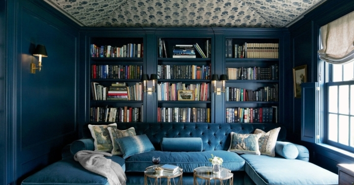 decoracion salon en azul, estanterias originales, sofá tapizada de terciopelo, librería de madera masiva de suelo a techo, techo con papel pintado