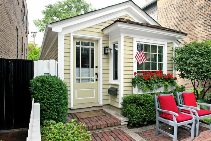 mini casas de ensueño, casa de diseño clásico de pequeño tamaño pintada en color ocre y blanco, pequeño jardín con sillas cómodas
