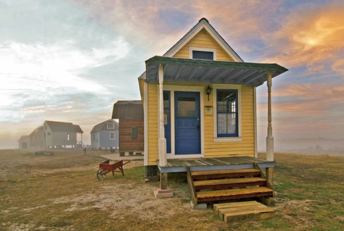 mini casa, pequeña casa en color amarillo con puerta azul, veranda de madera con escaleras, pequeña buhardilla habitable
