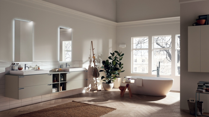 espacio con luz natural baño en tonos neutrales, bañera exenta, baños pequeños, dos lavabos, dos espejos, plantas verdes, tapete, suelo con parquet, ventana grande