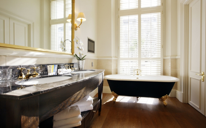 decoración moderna, baños pequeños, lavabo con encimera de mármol, bañera con partas de garra doradas, espejo grande, ventanal con persianas, suelo laminado