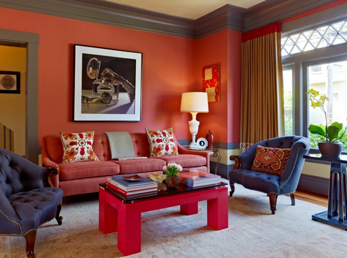 decoración clásica con paredes rojas, salón con ventanas grandes y cortinas masivas, mesa roja con revistas, flores, sillónes tapizados en capitoné azules