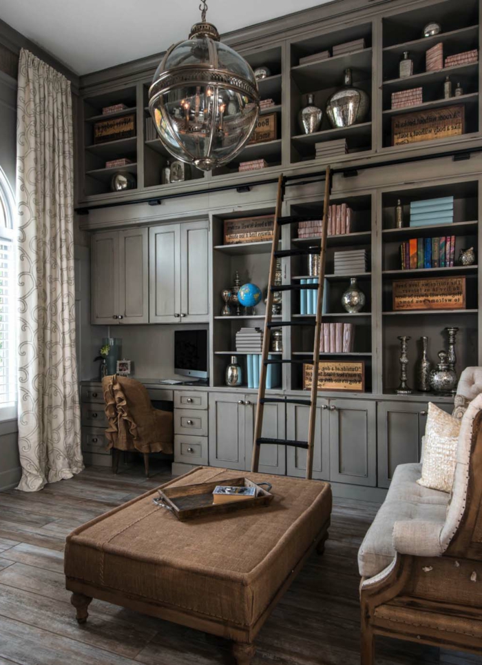 habitación despacho, librerias, armario con estantes y escritorio de madera gris, escalera de mano, sofá y mesa tapizados, suelo con tarima, lámpara colgante
