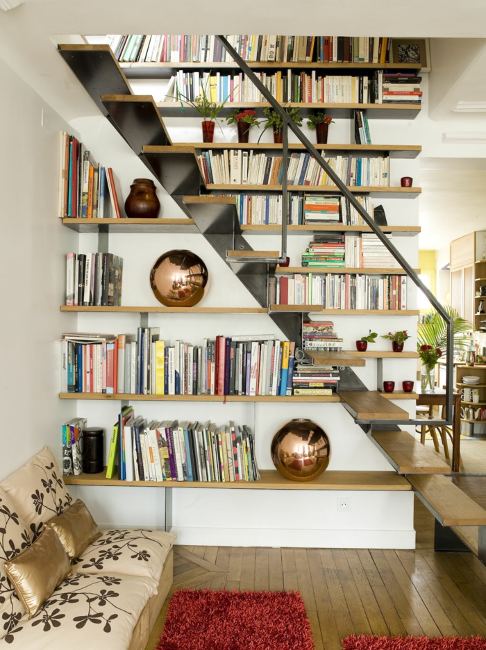 escalera de metal y madera, rincón de lectrua, baldas de madera, sofá pequeño en beige y forado, tapete rojo, librería con jarrones decorativos