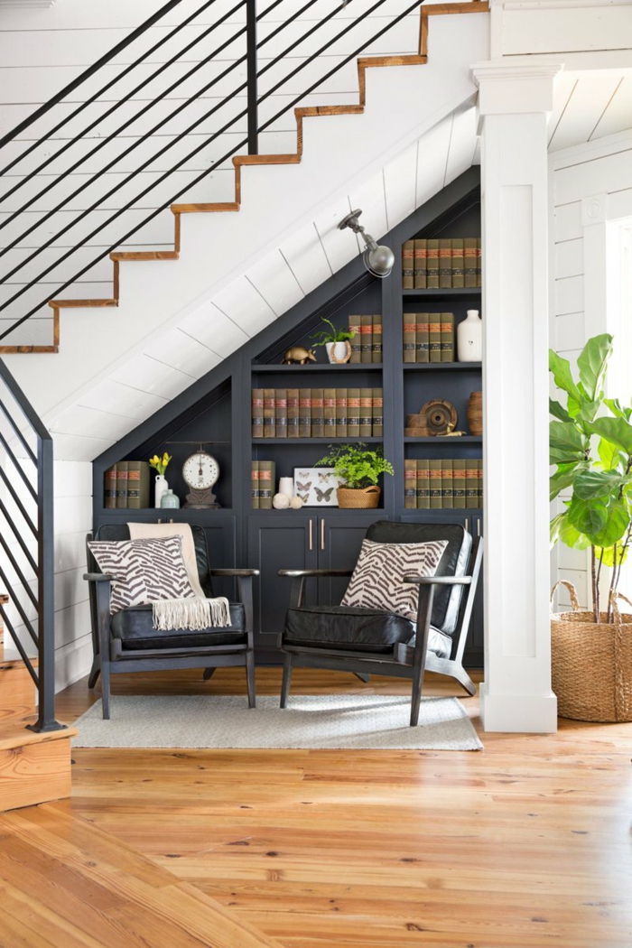 decoración moderna, casa con escalera, sillones de piel con cojines tipo zebra, librería de madera azul navy, suelo con parquet, planta verde