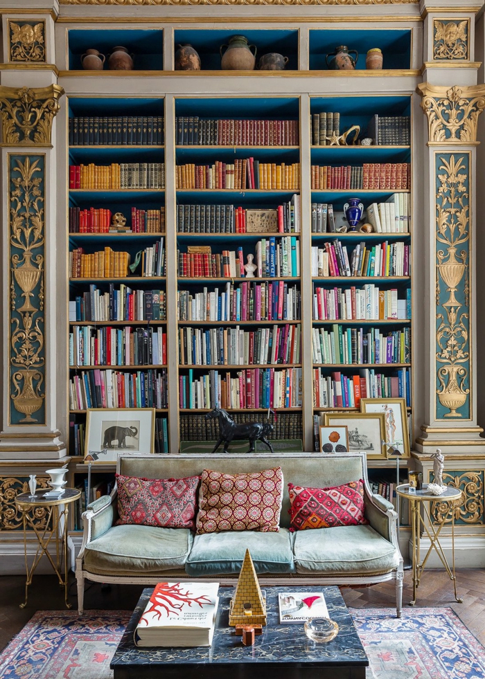 estanterias para libros, salón vintage con librería empotrada, decoración de pared con figuras en dorado, jarrones de barro, mesa de mármol, sofá con cojines, alfombra con aspecto antiguo