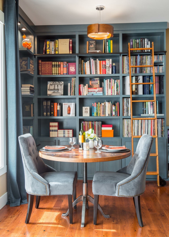 comedor para dos personas, estanterias para libros, decoración en azul grisáceo, mesa redonda, librería con escalera de mano madera