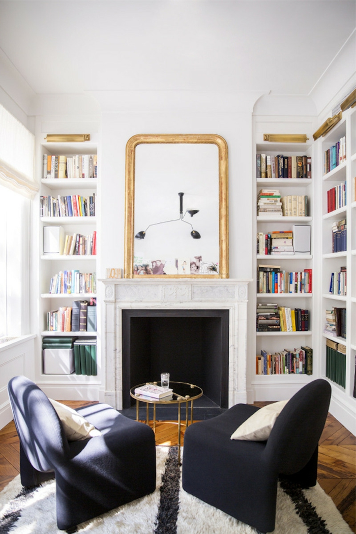 salón con librerías empotradas, chimenea con espejo grande en marco color dorado, estanterias de pared, suelo de parquet, sillones negros