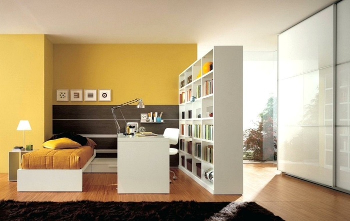 separar ambientes, grande salón con paredes en color mostaza, muebles modernos de madera, separador de ambientes en forma de biblioteca
