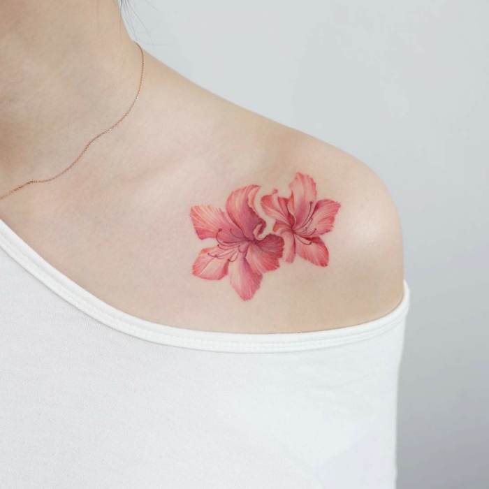 tatuaje hombro, tatuaje femenino en la clavícula, flor de hibisco en rosado, mujer con blusa branca de hombro caído