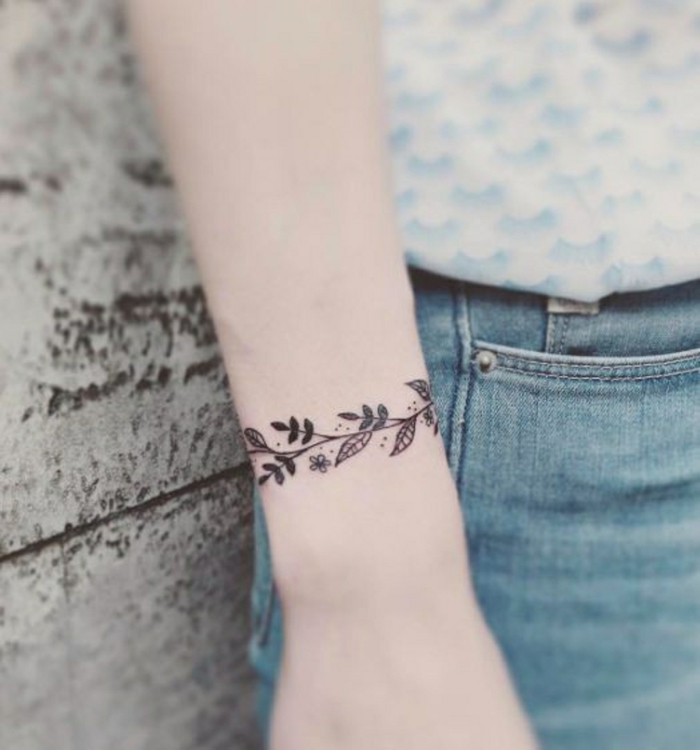 tatuaje femenino como brazalete en la muñeca, motivos florales, blanco y negro, mujer en jeans, tatuajes flechas