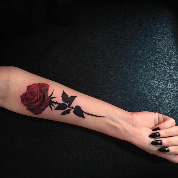 tatuaje muñeca, mujer con tatuaje en el antebrazo, manicura con uñas largas y esmalte oscuro, rosa con tallo y hojas negras