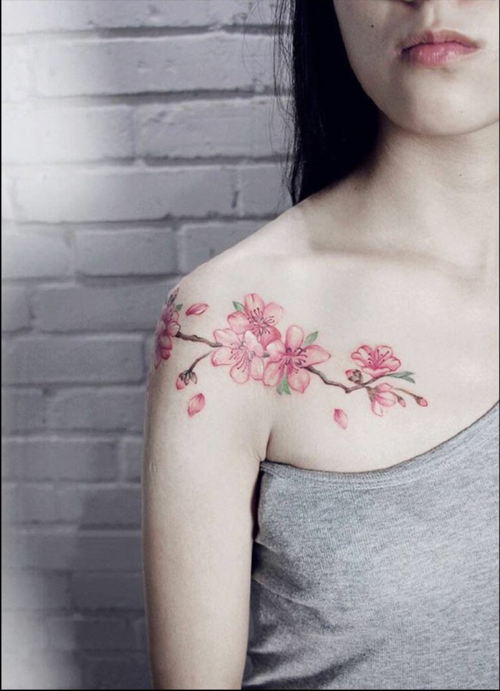 tatuaje hombro, mujer flaca con blusa gris, tatuaje de flor de cerezo en hombro y clavícula, color rosa