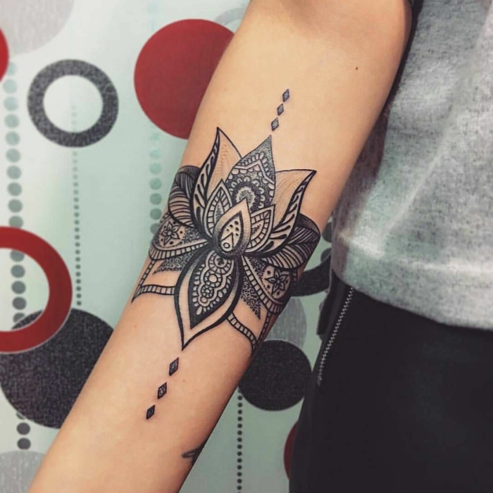 tatuaje pequeño, tatuaje en el antebrazo de mujer, flor de loto con motivos orientales en blanco y negro, tatuaje brazalete