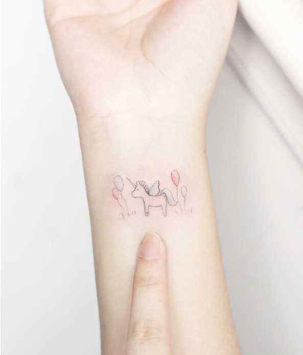 tatuaje para mujeres con dibujo infantil de unicornio con globos, colores pálidos rosado y azul, tatuajes flechas, diseño minimalista 