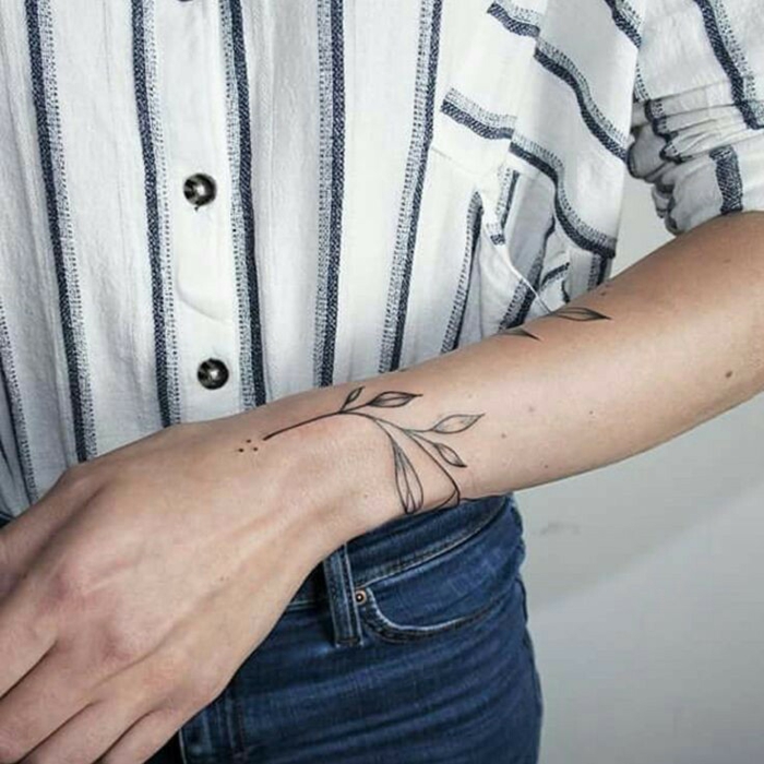 mujer con camisa en rayas blanco y negro y jeans, tatuaje con hojas en la muñеca y el antebrazo, tatuajes originales