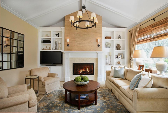 combinacion de colores, salón rústico con chimenea, techo blanco triangular, paredes beige, mesa redonda de madera, sofá y sillones tapizados beige con cojines, alfombra
