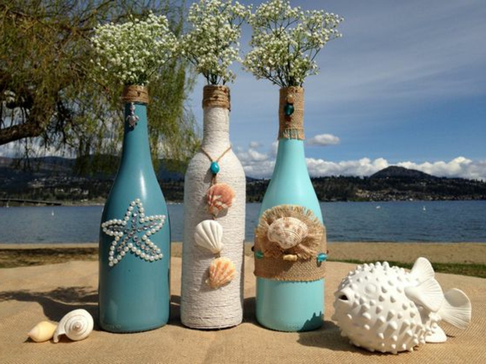 bonita propuesta para jarrones DIY, ideas con botellas de vino recicladas, botella de agua dibujo decorada con conchas e hilo cañamo 
