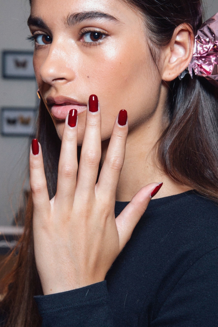 tendencias en diseños de uñas, uñas largas pintadas en rojo bordeos, forma ovalada, mujer con pelo castaño largo 
