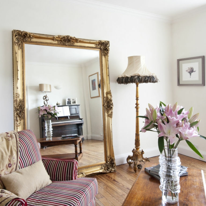 preciosa sala de estar con grande espejo dorado apoyado en la pared, decoración con espejos en estilo vintage y bonitas flores 