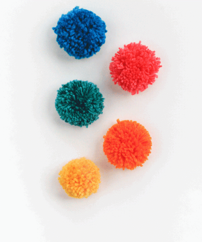 cinco pompones en amarillo, azul, rojo, naranja y verde, grandes bolas de lana en colores, manualidades con pompones paso a paso 