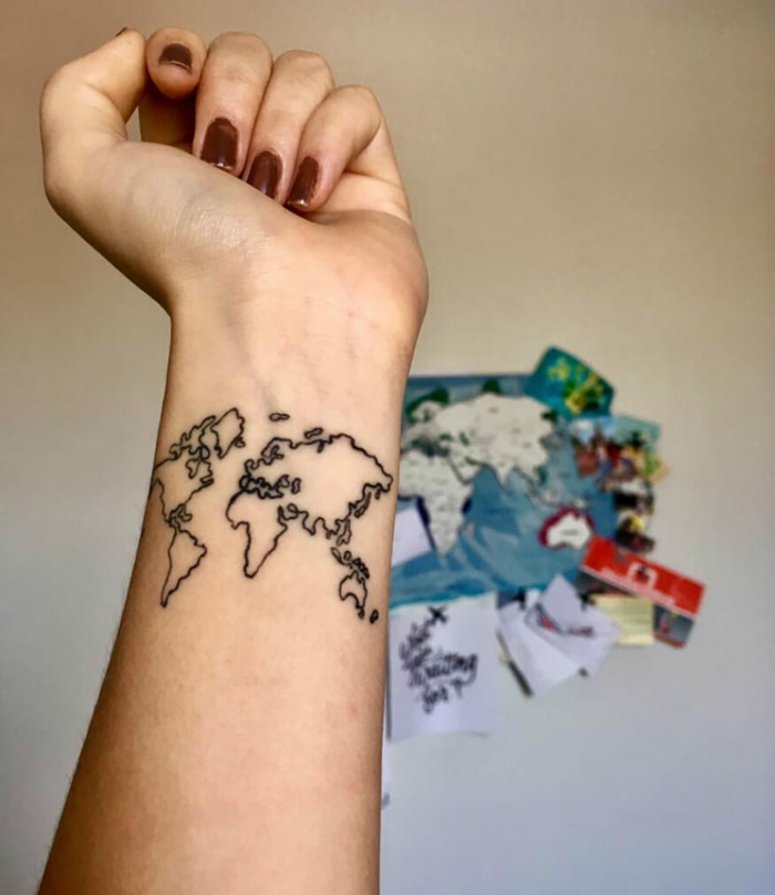 mano de mujer, uñas pintadas en carmín, tatuaje de nombres en la muñeca, mapa mundo de líneas negras, fondo con mapa en la pared
