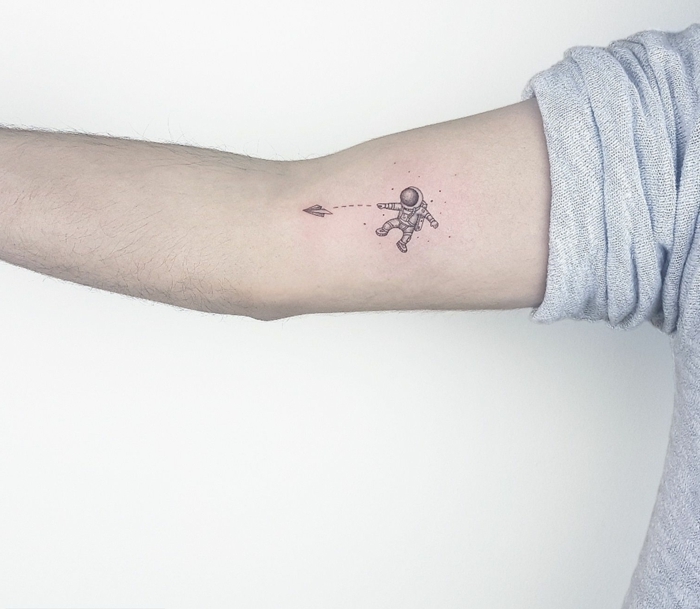 idea de diselo de tatuaje para el brazo, tatuajes minimalistas, astronauta con papel de avion, brazo de hombre
