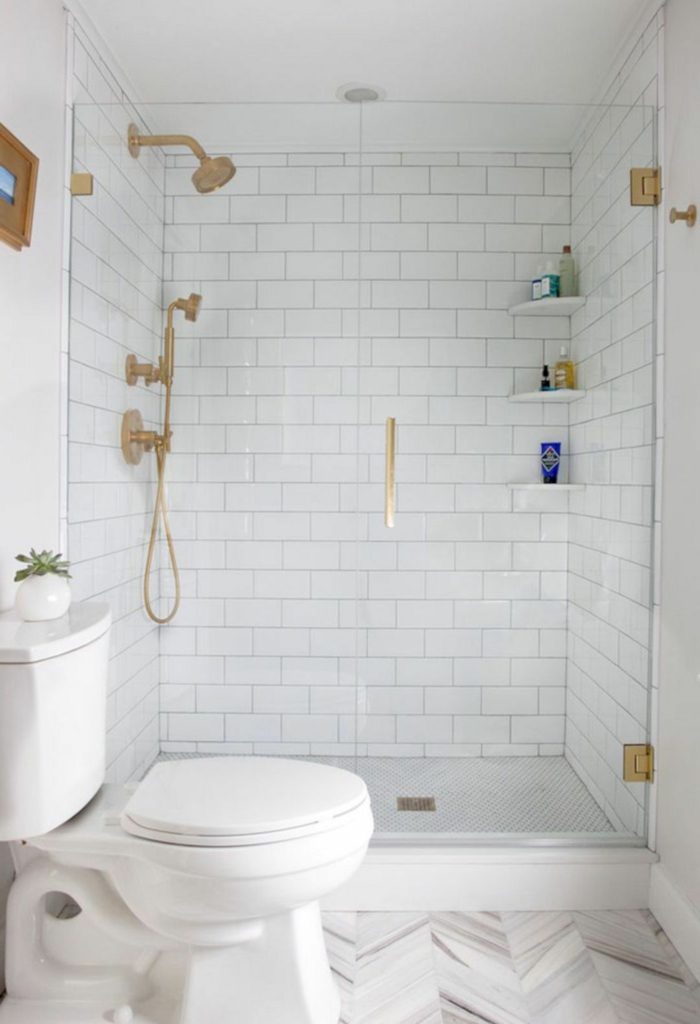 baño decorado en blanco con acentos en dorado, luz natural, ducha de obra con puerta de vidrio, baños pequeños con ducha