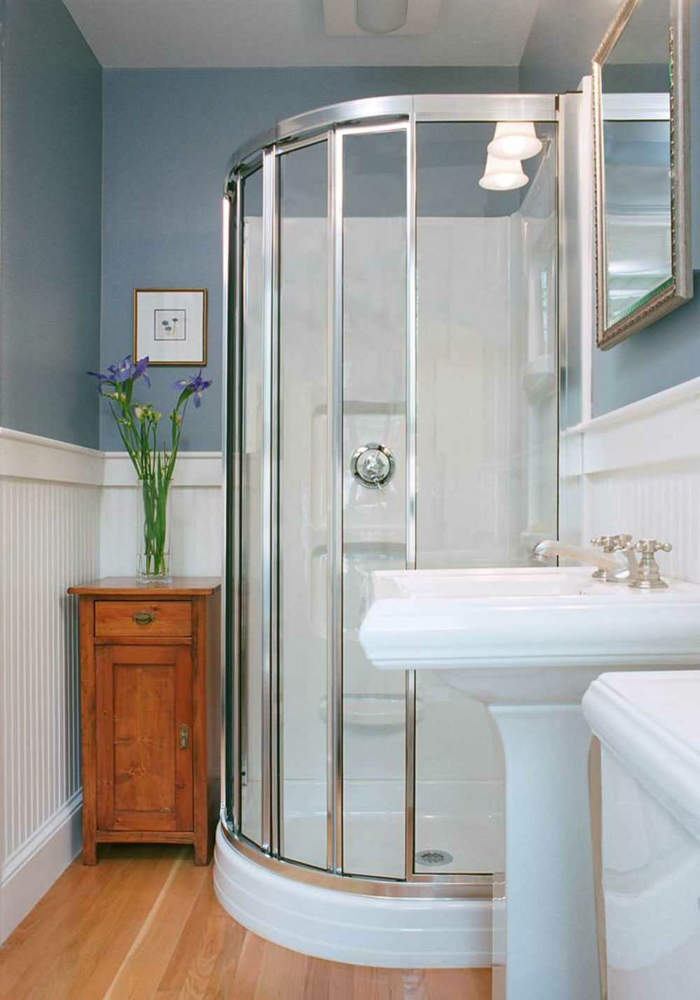 cabina de ducha con marcos de metal, suelo laminado, armario pequeño con flores, paredes en azul y blanco, espejo rectangular, decoracion baños pequeños