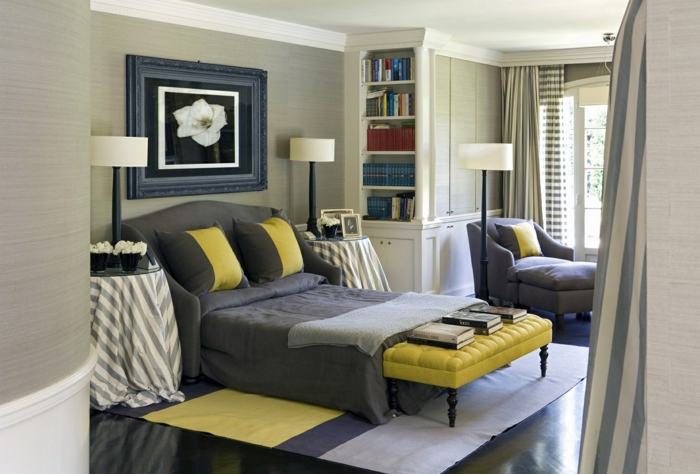 dormitorio grande moderno, habitacion gris, pie de cama de cuero en capitoné, cuadro con lirio, tapete en suelo lamiando, sillón y ventana grande