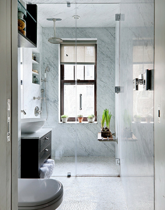 baño con ducha y ventana grande decorada con siemprevivas, paredes de mármol, suelo de mosaico, ducha efecto lluvia, baños modernos