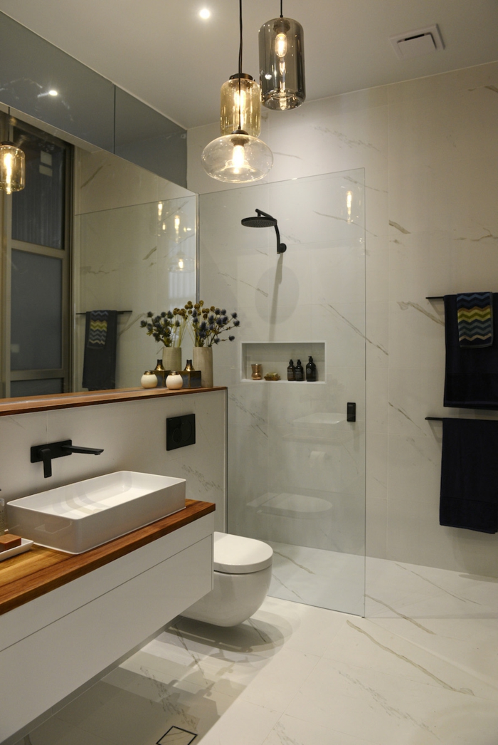 baño moderno pequeño, decoracion con marmol y lamparas colgantes, ducha de obra con nichos en la pared, espejo grande, baños modernos