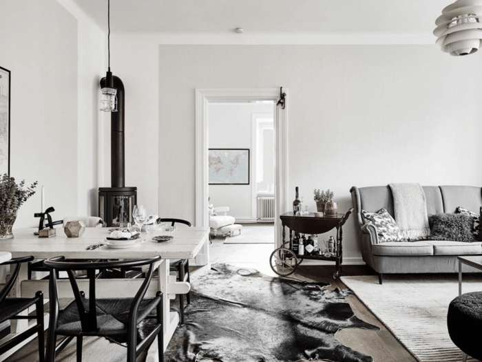 decoración en blanco y negro, salon nordico on chimenea y alfombra piel de vaca, sofá gris, mesa para cuatro, lámpara colgante
