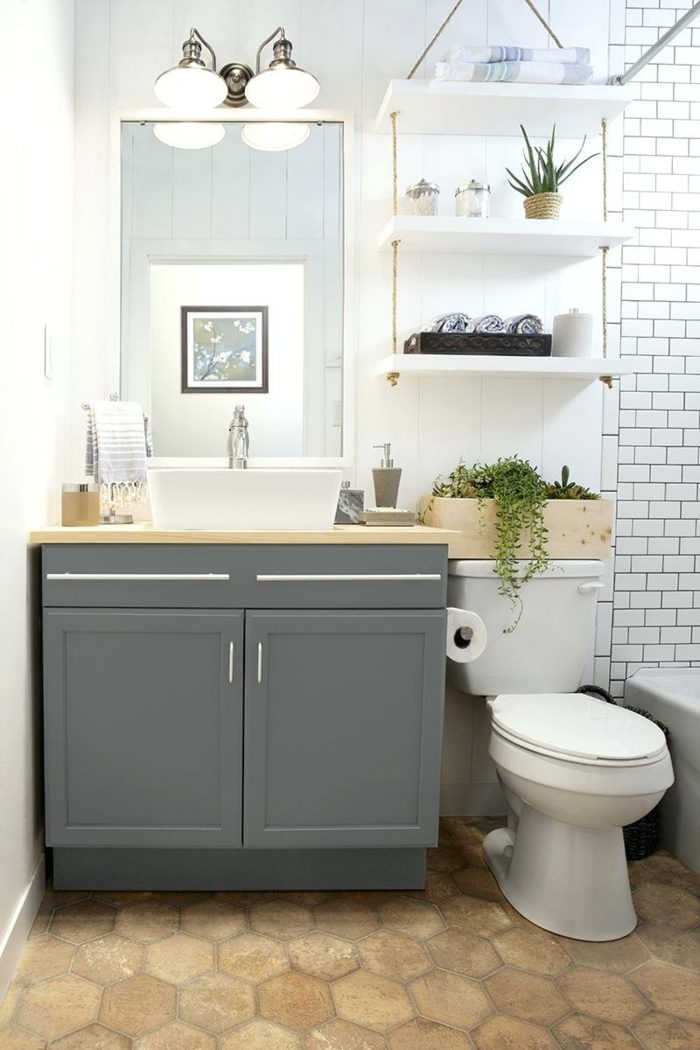 estilo moderno, mueble lavabo con puertas de madera gris, ducha con bañera, estantería de cuerda y madera con plantas verdes, espejo grande, cuartos de baño pequeños
