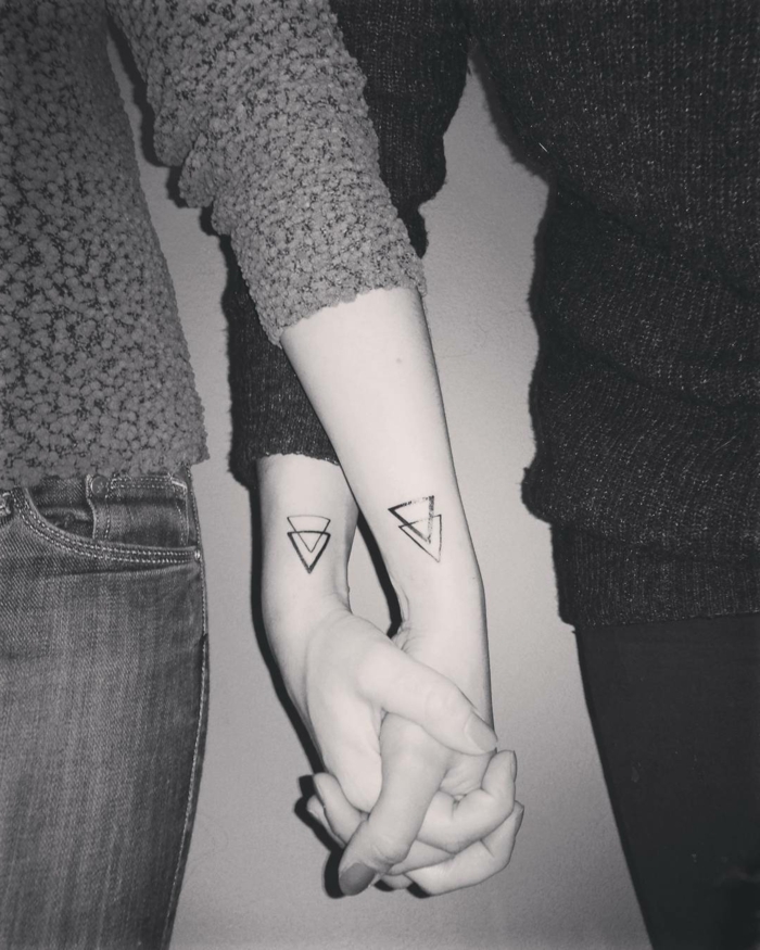 tatuajes geométricos para hermanas o amigas, mujeres mano en mano, tatuaje en la muñeca triángulos entrelazados, foto en blanco y negro, mujeres con jersey