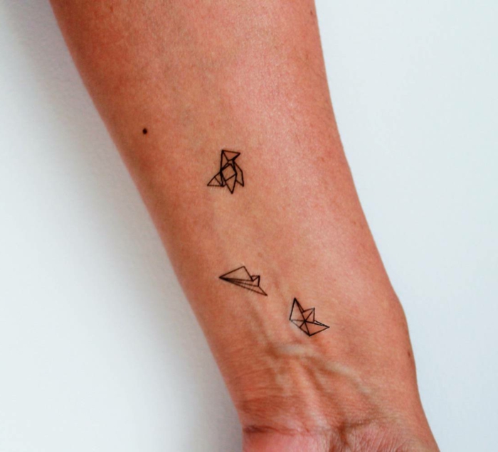 tatuajes inspirados en origami, antebrazo con tatuaje de figuras de papel, perro, gorro y avion, tatuajes originales