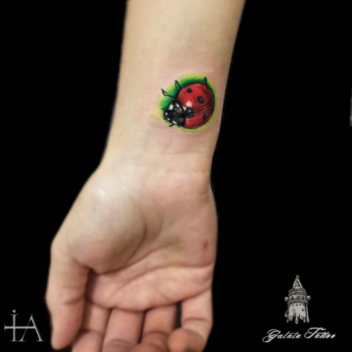 tatuajes en la muñeca, diseño de tattoo pequeño de color, mariquita en rojo y verde, parte interior de la muñeca