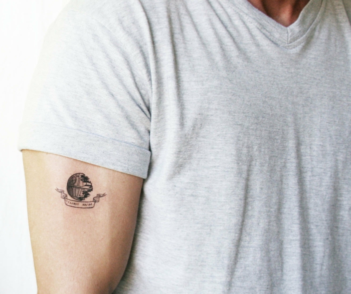 hombre con brazo musculoso, tatuaje pequeño de imagen y frase, camiseta gris, tatuajes simbolicos