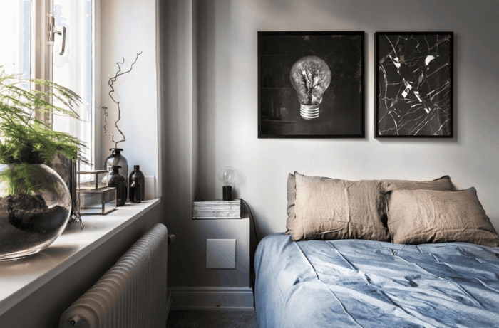 dormitorio nordico, espacio pequeño, ventana con plantas verdes, cuadros en blanco y negro, ropa cama en azul grisáceo y beige