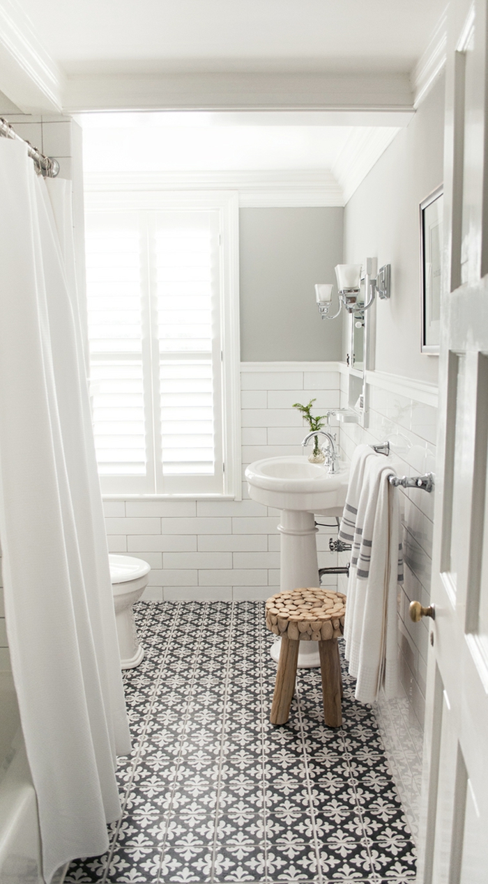 baño pequeño con mucha luz, decoracion en blanco y gris, duchas de obra, suelo con baldosas de patron floral, taburete de madera, ducha con cortina