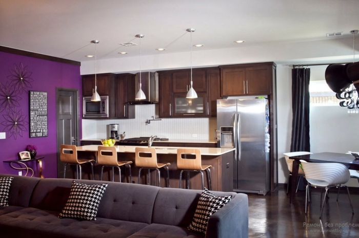 sala de estar moderna con cocina abierta, pared en color lila con decoracion como punto focal, pequeño comedor 