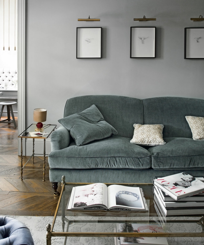 salon pequeño, sofá tapizado en terciopelo, mesa de vidrio, bocetos enmarcados, suelo con parquet y alfombra, habitación gris