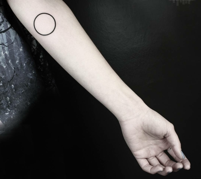 tatuajes chicos, antebrazo delgado de mujer con anillo, tatuaje pequeño, círculo de tinta negra, figuras geometricas
