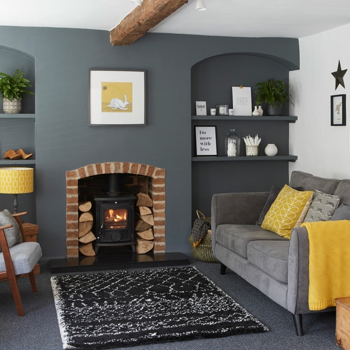 salon en gris pizarra y amarillo, chimenea encendida, techo con vigas de madera, como decorar una habitacion, moqueta y alfombra, nichos con estantes