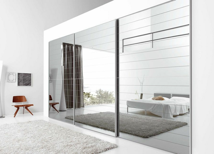 dormitorio luminoso decorado en blanco en estilo minimalista, decoración de espejos plateados, alfombra peluda en blanco 