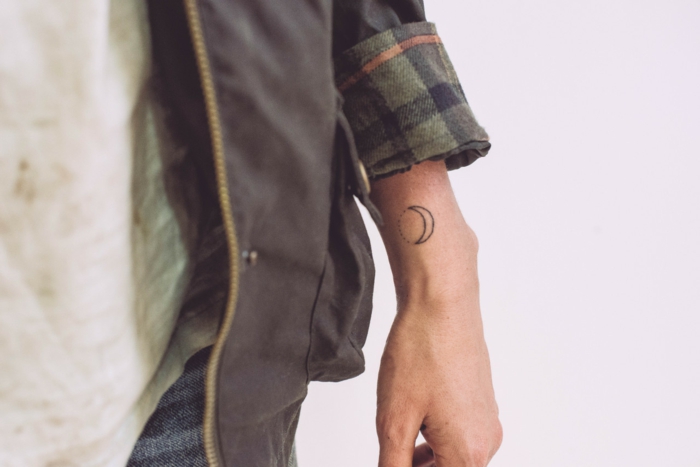 mini tatuajes, hombre con muñeca tatuada con media luna, estilo geométrico, chaqueta con mangas largas