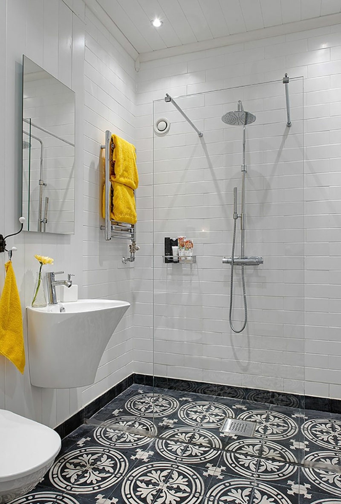 baño en blanco y negro, accesorios en amarillo, duchas de obra, mampara de vidrio, baldosas con patron floral, luces empotradas en el techo
