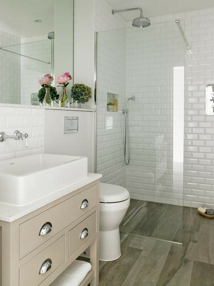 baños pequeños con ducha, combinación blanco con color crema, espejo grande, decoracion con flores, pared de ladrillo visto esmaltado, ducha con mampara de vidrio, suelo con tarima