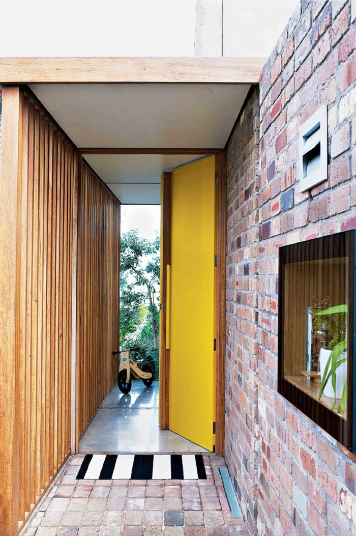 recibidor moderno con paredes de ladrillo, puerta pintada en amarillo y estantería con plantas verdes 
